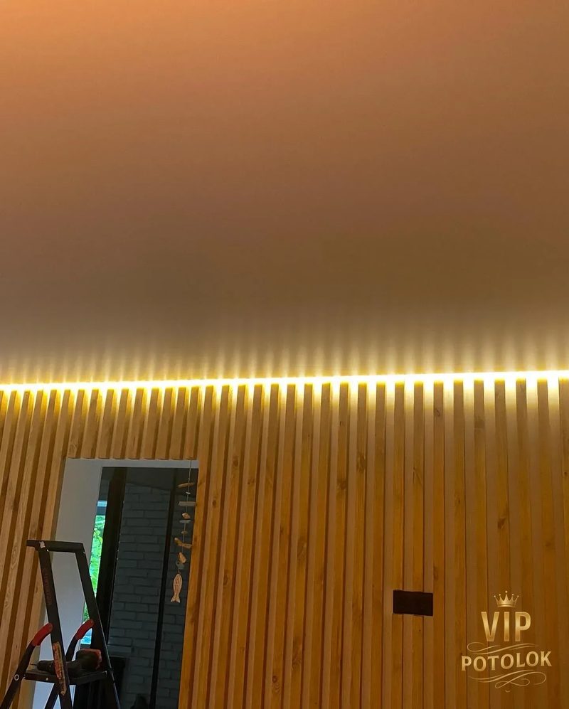 Тепла LED-підсвітка вздовж дерев’яної рейкової стіни під матовою стелею